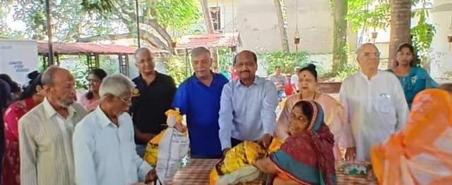Dignitaries outdoors presenting sweets and clothing during Diwali